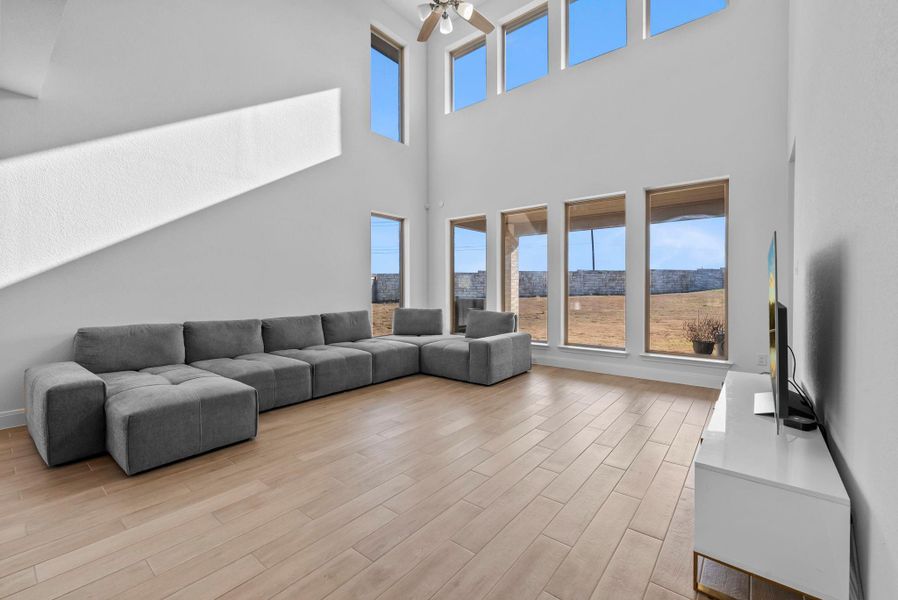 Living room featuring light wood-style floors, ceiling fan, and a towering ceiling