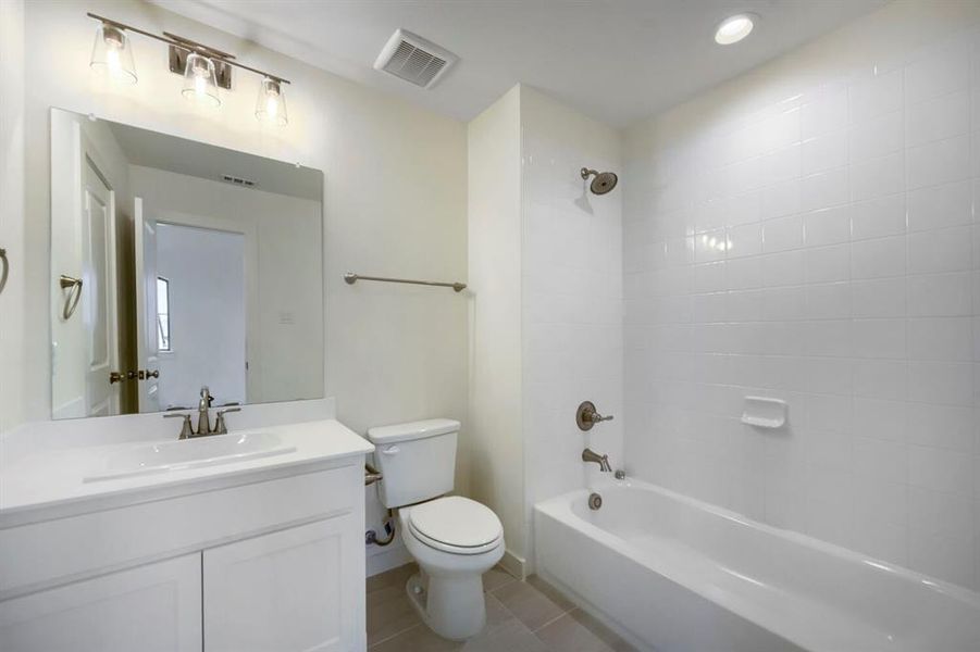 Bathroom featuring a white vanity with integrated sink, brushed nickel fixtures, a rectangular mirror, a toilet, and a bathtub with white subway tile surround Bathroom featuring a white vanity with integrated sink, brushed nickel fixtures, a rectangular mirror, a toilet, and a bathtub with white subway tile surround