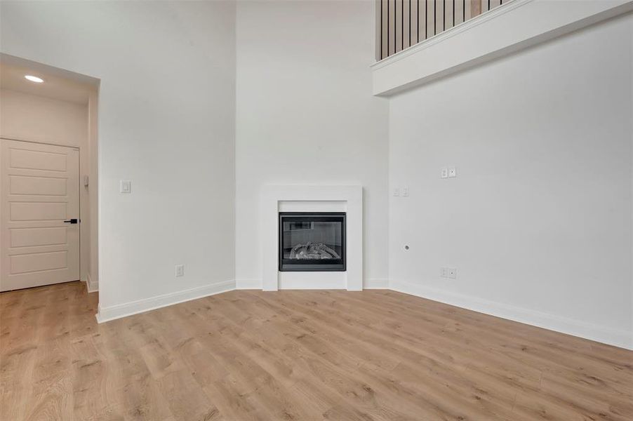 Unfurnished living room featuring a high ceiling, a glass covered fireplace, and light wood-style floors