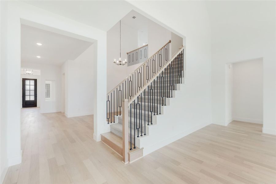 Open foyer with wood and iron staircase, light hardwood floors, and chandelier overhead