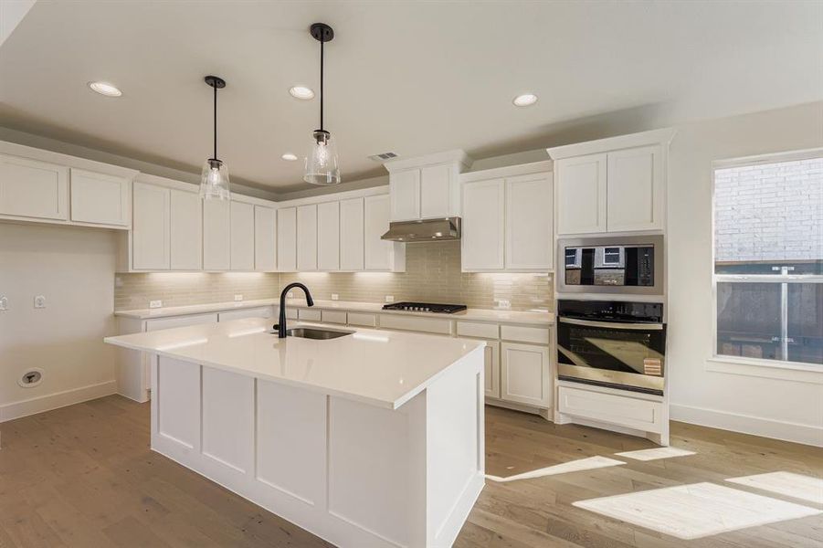 Kitchen featuring stainless steel appliances, white cabinetry, hanging light fixtures, a center island with sink, and backsplash Kitchen featuring stainless steel appliances, white cabinetry, hanging light fixtures, a center island with sink, and backsplash