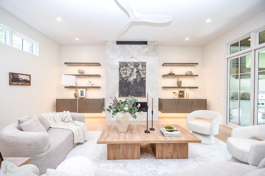 This bright, modern living room features a cozy seating area with plush sofas and chairs. It has a sleek, minimalist design with built-in shelving, a central coffee table, and large windows letting in plenty of natural light. Perfect for relaxation and entertaining.