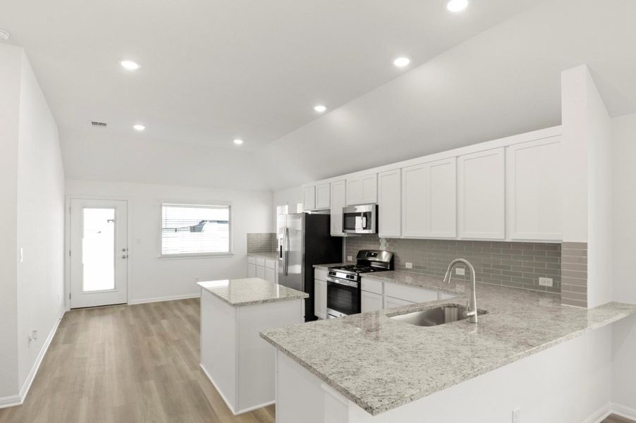 Kitchen with a center island, white cabinets, appliances with stainless steel finishes, tasteful backsplash, and vaulted ceiling