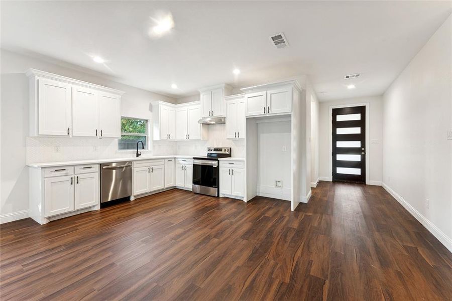 Kitchen with stainless steel appliances, white cabinetry, dark wood-type flooring, tasteful backsplash, and recessed lighting