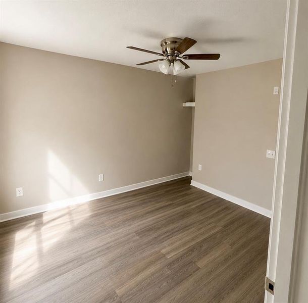 Spacious room featuring wood-finish flooring, neutral-toned walls, and white baseboards Spacious room featuring wood-finish flooring, neutral-toned walls, and white baseboards