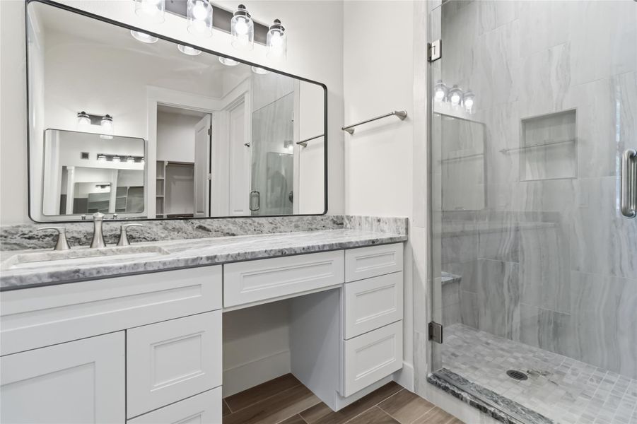 Primary ensuite with separate vanities and walk-in shower with bench seat and frameless glass