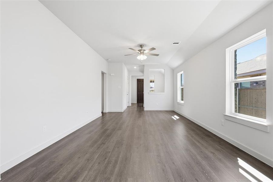 Unfurnished living room with healthy amount of natural light, dark wood finished floors, ceiling fan, and vaulted ceiling
