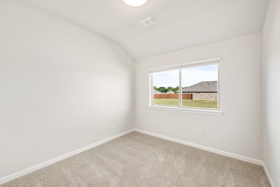 Empty bedroom with vaulted ceiling, beige carpet, and a window overlooking the backyard