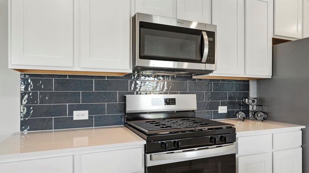 Kitchen with appliances with stainless steel finishes, white cabinets, and decorative backsplash