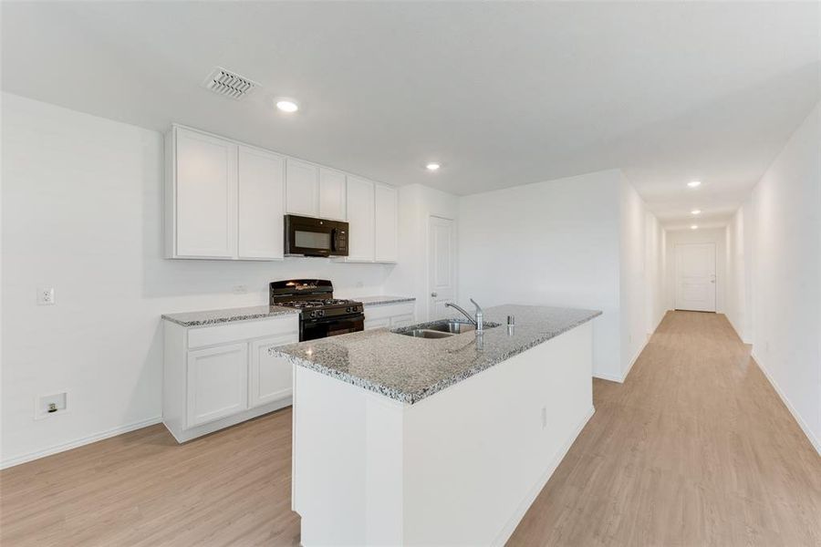 Kitchen with light hardwood / wood-style flooring, a center island with sink, white cabinetry, and black appliances