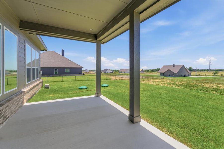 Covered concrete patio featuring recessed lighting, a brick and siding exterior, large windows, and an expansive grass area