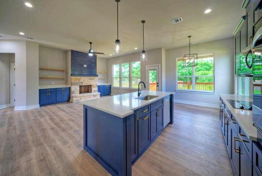A seamless flow connects the open-concept kitchen and living area, highlighted by a bold blue kitchen island and a stone fireplace.
