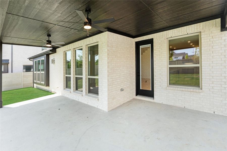 Covered back patio with ceiling fans, concrete floor, and white brick exterior with black door and large windows Covered back patio with ceiling fans, concrete floor, and white brick exterior with black door and large windows