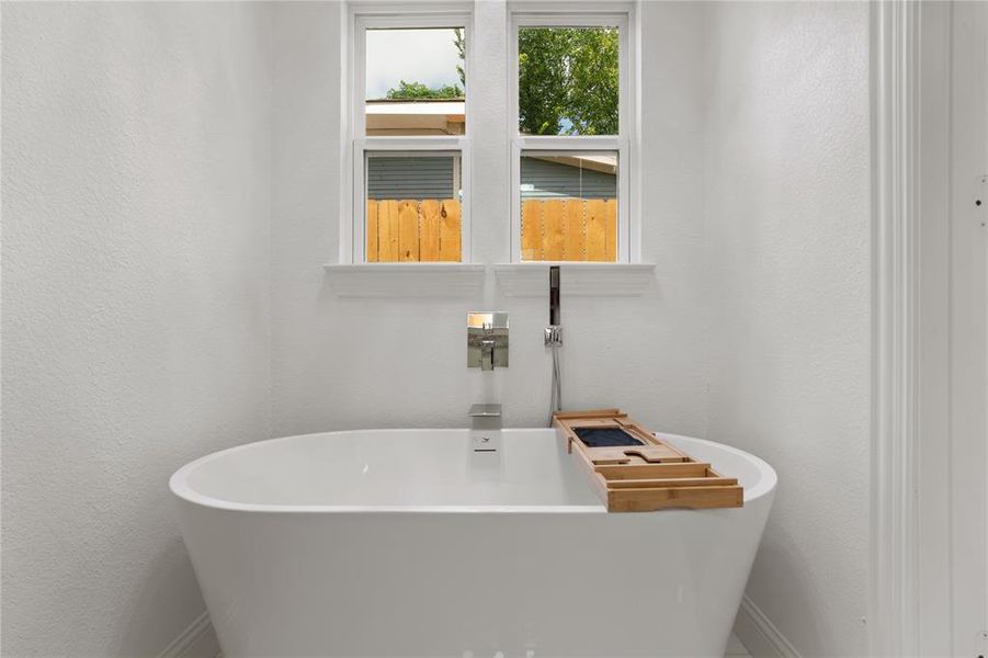 Freestanding soaking tub with a wall-mounted chrome faucet and handheld shower sprayer