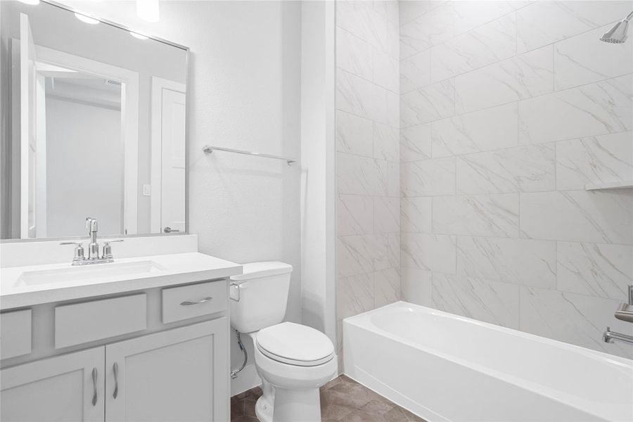This well appointed secondary bathroom features stained cabinetry, white quartz countertop, tub/shower combination with tile surround, and sleek modern hardware.