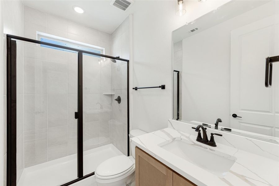 Bathroom with glass walk-in shower, white tile walls, quartz vanity countertop, and black fixtures