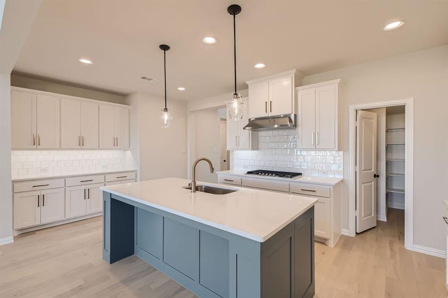 Kitchen with sink, light wood-type flooring, an island with sink, hanging light fixtures, and white cabinets