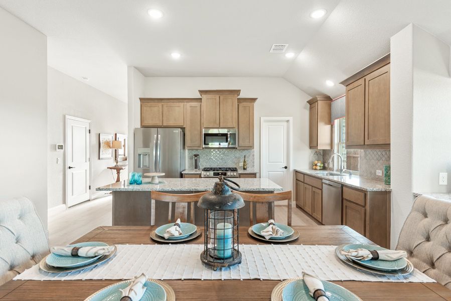 Open-concept kitchen and dining area with brown cabinets, granite countertops, stainless appliances, and a set dining table in the foreground. Open-concept kitchen and dining area with brown cabinets, granite countertops, stainless appliances, and a set dining table in the foreground.