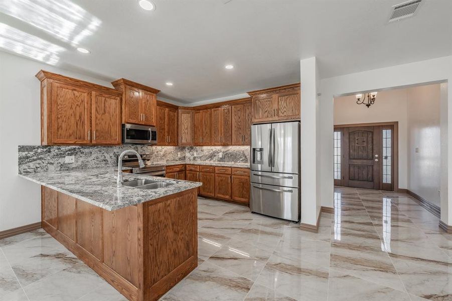 Kitchen with marble finish floor, stainless steel appliances, brown cabinetry, a sink, and a peninsula