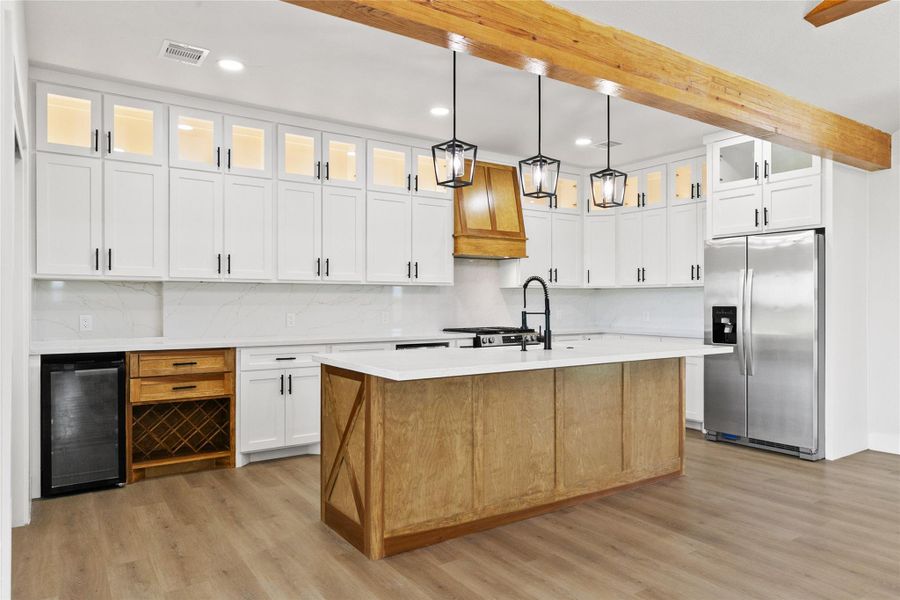 The kitchen blends style and function with quartz countertops, a wood island with an apron-front farmhouse sink, beverage refrigerator, wine storage, under-counter microwave, lighted glass-front cabinetry, and a large walk-in pantry.