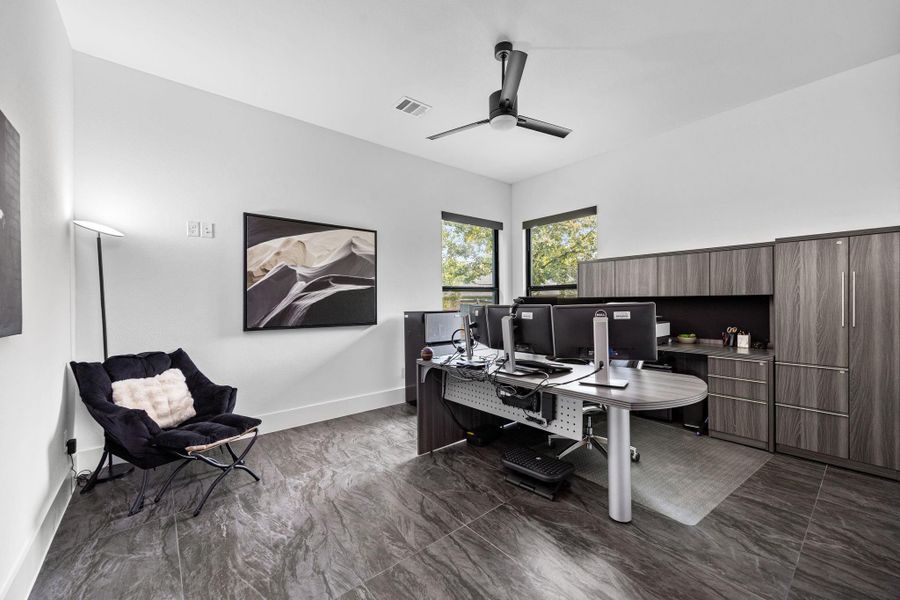 This is a modern home office has sleek, dark flooring and two windows for natural light. This is a modern home office has sleek, dark flooring and two windows for natural light.