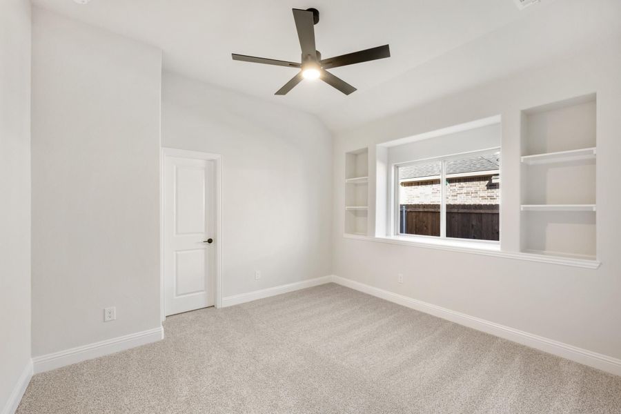 Empty bedroom with carpet, vaulted ceiling, ceiling fan, and built-in wall shelves flanking a window