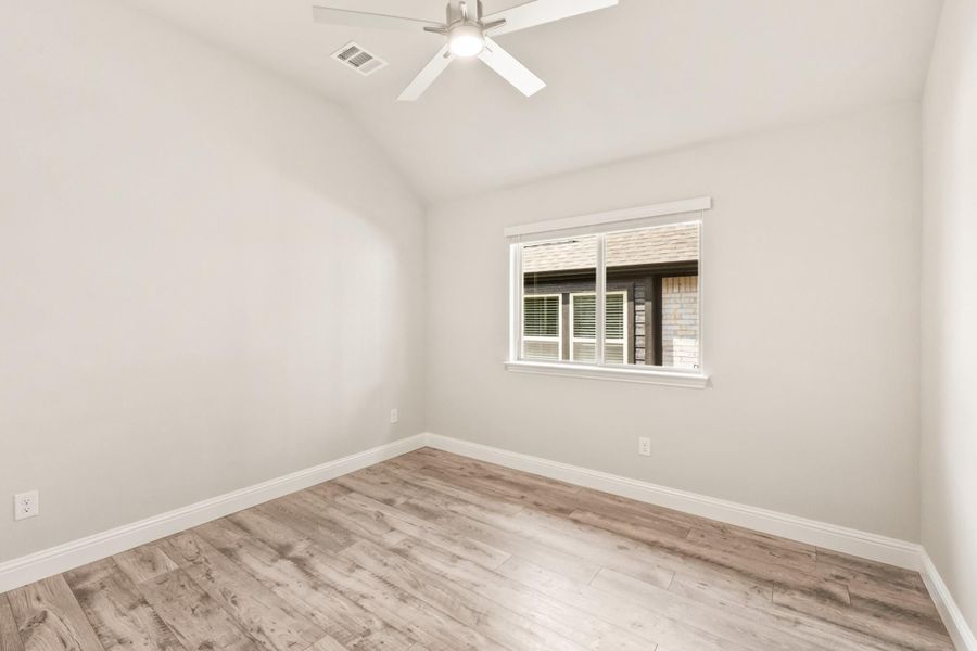 Empty bedroom with light wood floors, ceiling fan, vaulted ceiling, and single window Empty bedroom with light wood floors, ceiling fan, vaulted ceiling, and single window