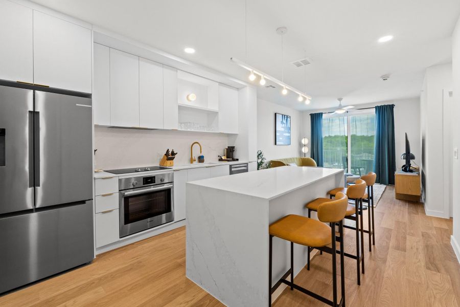 Shown in the Skylark palette, this kitchen features white cabinetry, brass hardware, quartz countertops with subtle veining, and Bosch appliances. Residences come with a fully functional setup including cookware, dishes, and a coffee machine for everyday use. Shown in the Skylark palette, this kitchen features white cabinetry, brass hardware, quartz countertops with subtle veining, and Bosch appliances. Residences come with a fully functional setup including cookware, dishes, and a coffee machine for everyday use.