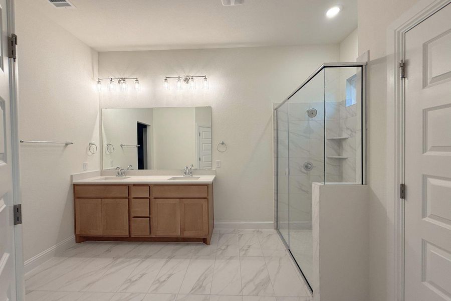 Bathroom with double vanity, light marble finish flooring, and a marble finish shower