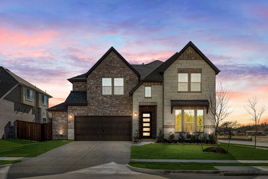 Two-story home with brick and stone exterior, two-car garage, and modern front door at dusk Two-story home with brick and stone exterior, two-car garage, and modern front door at dusk