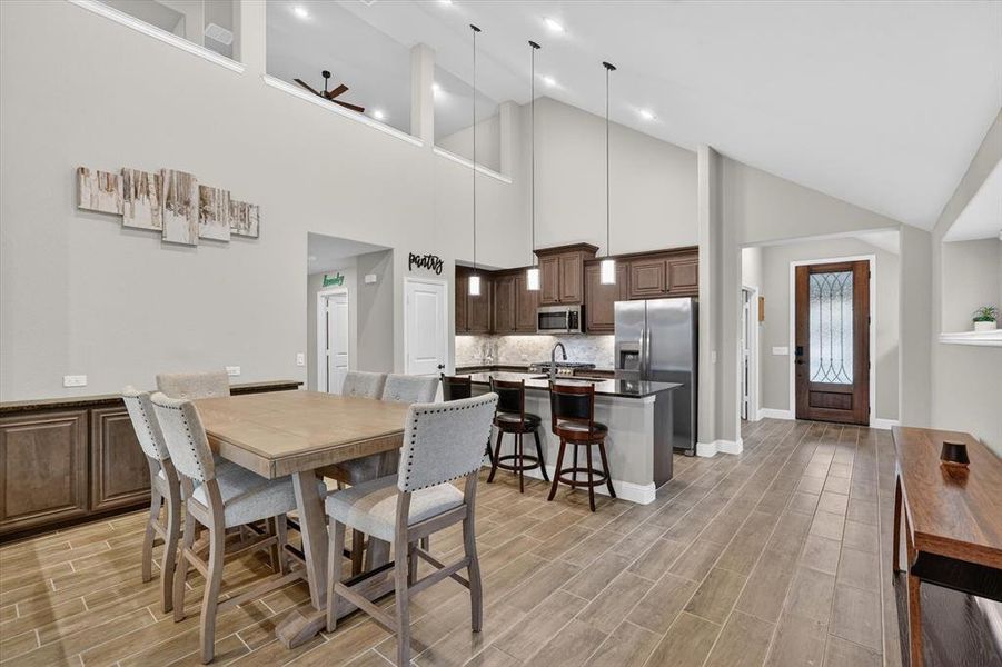Open-concept living space with vaulted ceilings, wood-finish flooring, a kitchen island, pendant lighting, and dark wood cabinetry Open-concept living space with vaulted ceilings, wood-finish flooring, a kitchen island, pendant lighting, and dark wood cabinetry