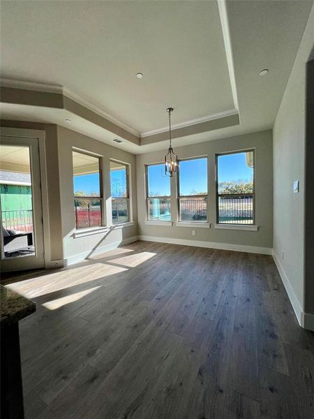 Unfurnished breakfast area featuring dark hardwood / wood-style floors, crown molding, a tray ceiling, and a notable chandelier