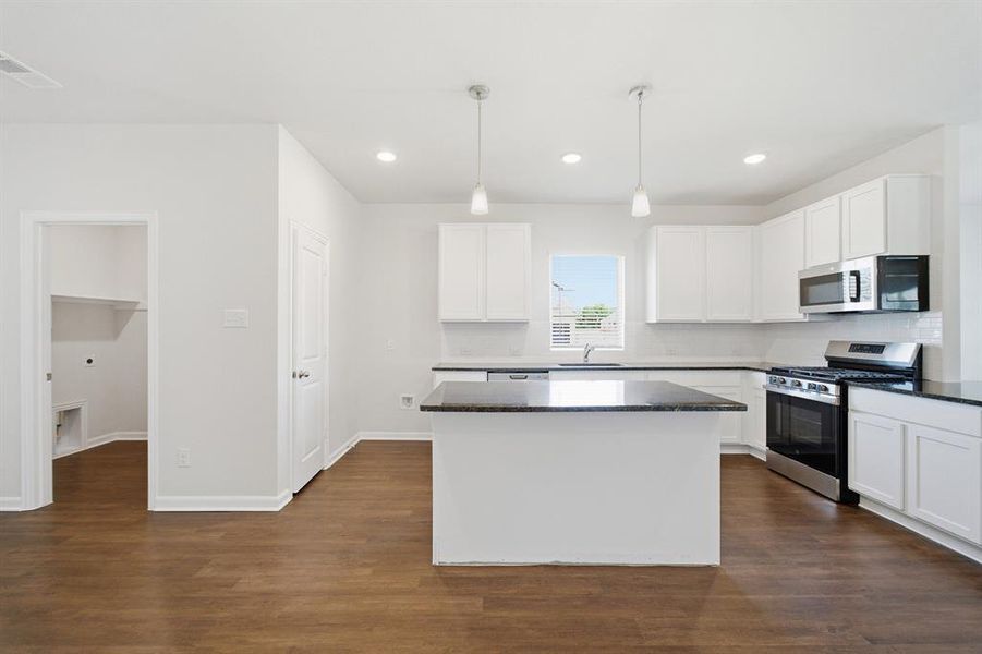 Modern kitchen featuring a central island with a dark countertop, white cabinetry, stainless steel appliances, and pendant lighting