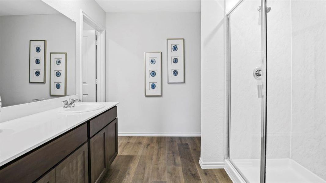 Bathroom featuring a single vanity with a white countertop, dark wood-finish cabinetry, a large wall mirror, and wood-finish flooring
