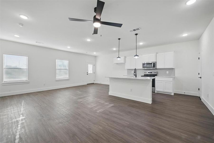 Kitchen with a ceiling fan, white cabinetry, appliances with stainless steel finishes, a center island with sink, and dark wood-style flooring Kitchen with a ceiling fan, white cabinetry, appliances with stainless steel finishes, a center island with sink, and dark wood-style flooring