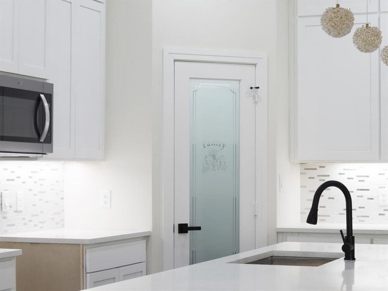Kitchen view of decorative backsplash, white cabinetry, stainless steel microwave, and light stone counters Kitchen view of decorative backsplash, white cabinetry, stainless steel microwave, and light stone counters