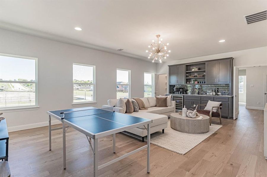 Playroom with beverage cooler, a chandelier, a wealth of natural light, and light hardwood / wood-style flooring