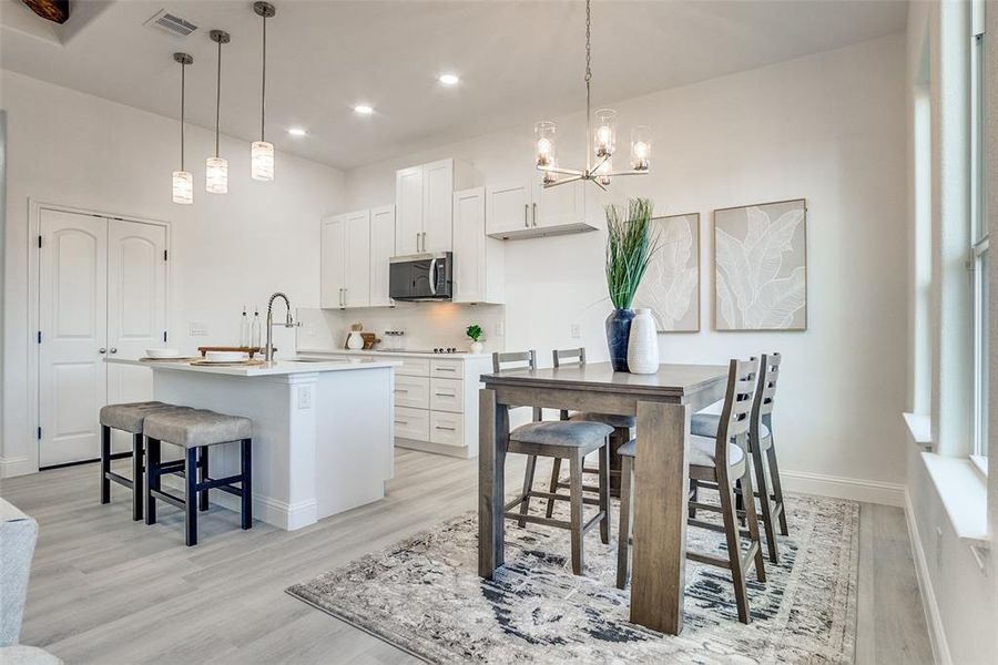 Kitchen with a breakfast bar area, white cabinetry, a chandelier, light wood finished floors, and tasteful backsplash Kitchen with a breakfast bar area, white cabinetry, a chandelier, light wood finished floors, and tasteful backsplash