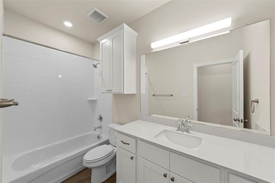 Bathroom featuring a white subway tile shower surround, a built-in white cabinet, a full-width mirror, a vanity with a white countertop and integrated sink, and wood-finish flooring