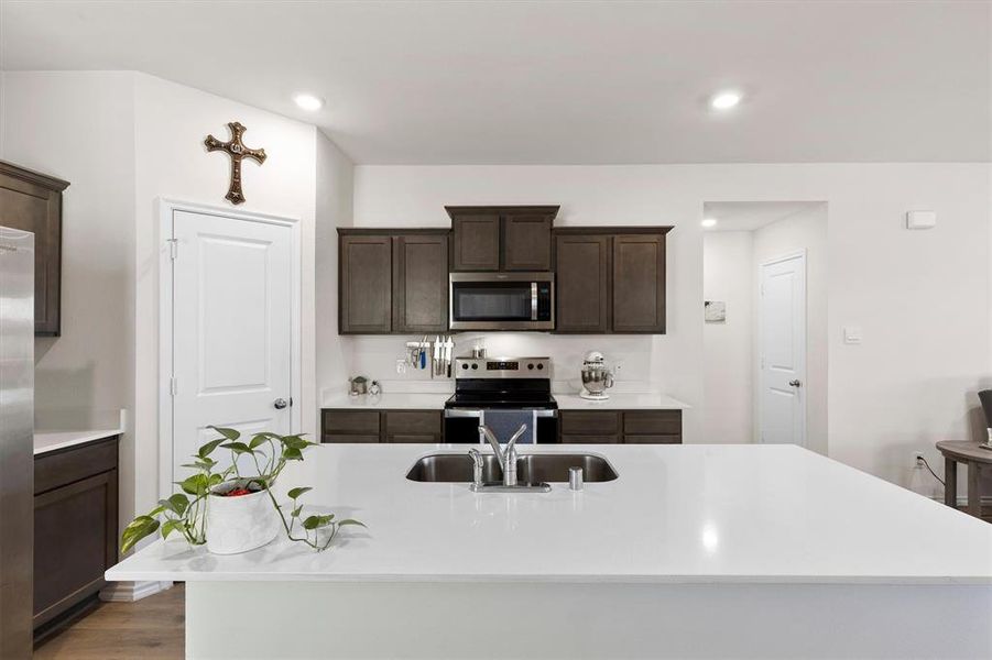 Kitchen with dark wood finish cabinetry, stainless steel appliances, an island with sink, light stone counters, and recessed lighting Kitchen with dark wood finish cabinetry, stainless steel appliances, an island with sink, light stone counters, and recessed lighting