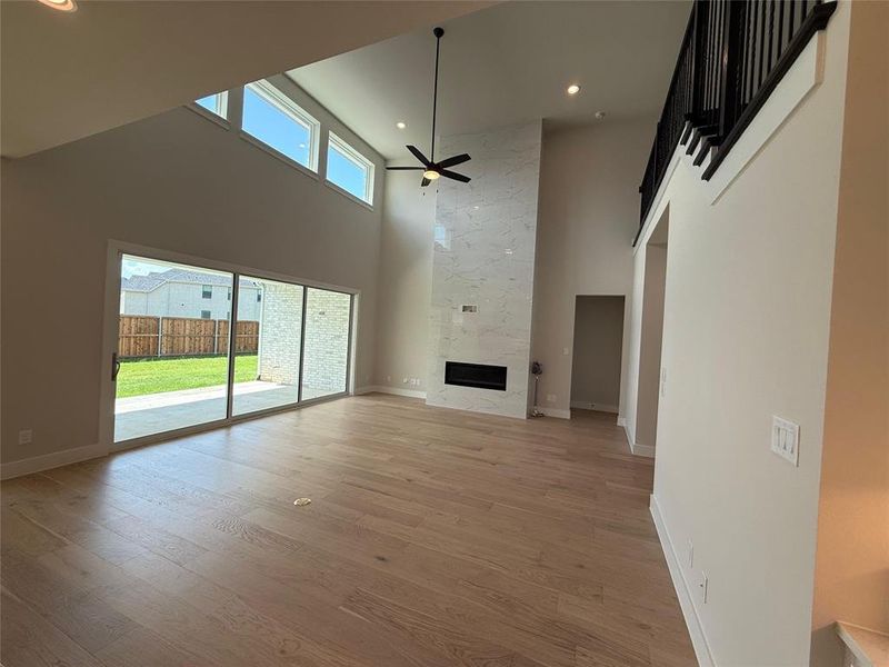 Unfurnished living room featuring a high end fireplace, a high ceiling, light wood-style floors, a ceiling fan, and recessed lighting Unfurnished living room featuring a high end fireplace, a high ceiling, light wood-style floors, a ceiling fan, and recessed lighting