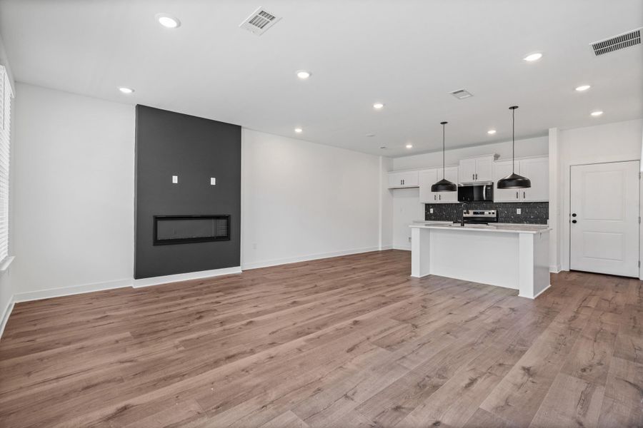 Wood-finish flooring, recessed lighting, and a linear fireplace with a dark accent wall Wood-finish flooring, recessed lighting, and a linear fireplace with a dark accent wall