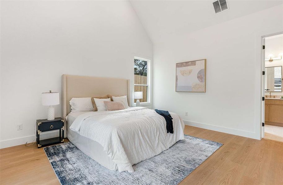 Bedroom featuring light wood-type flooring, ensuite bath, and high vaulted ceiling