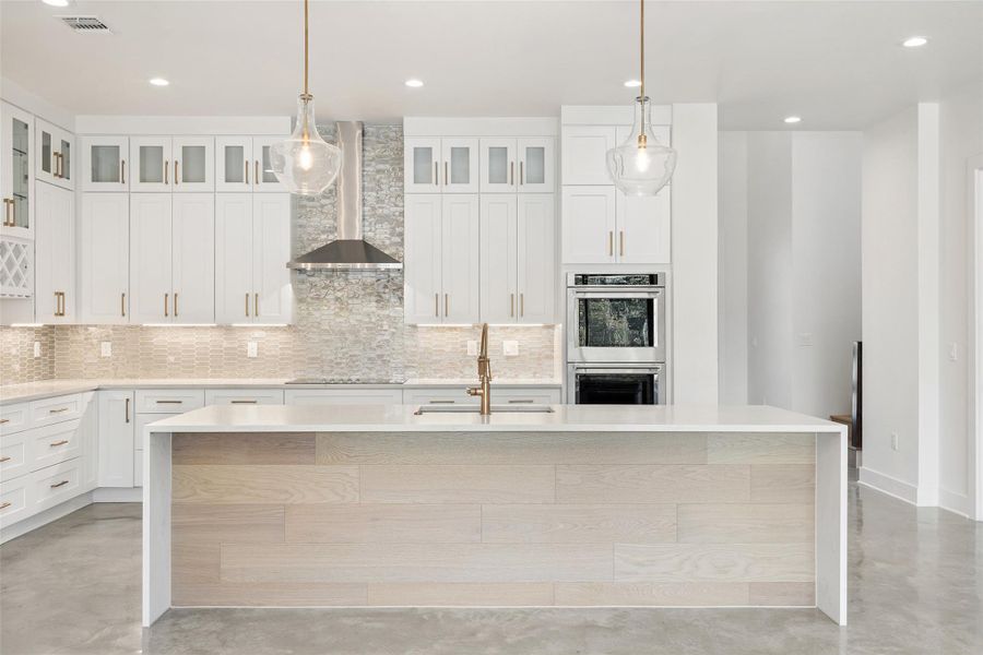Kitchen featuring concrete floors, hanging light fixtures, light stone counters, wall chimney range hood, and recessed lighting Kitchen featuring concrete floors, hanging light fixtures, light stone counters, wall chimney range hood, and recessed lighting