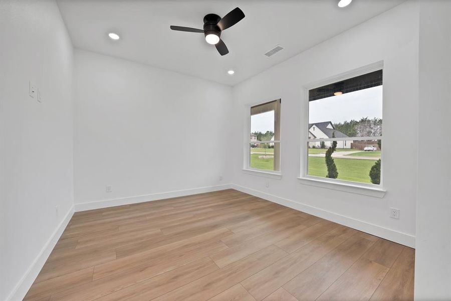 Spacious room featuring wood-finish flooring, crisp white walls, and a contemporary ceiling fan with integrated lighting