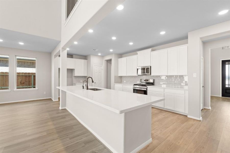 This light and bright kitchen features a large quartz island, white cabinets, a large sink overlooking your family room, recessed lighting, and beautiful backsplash.