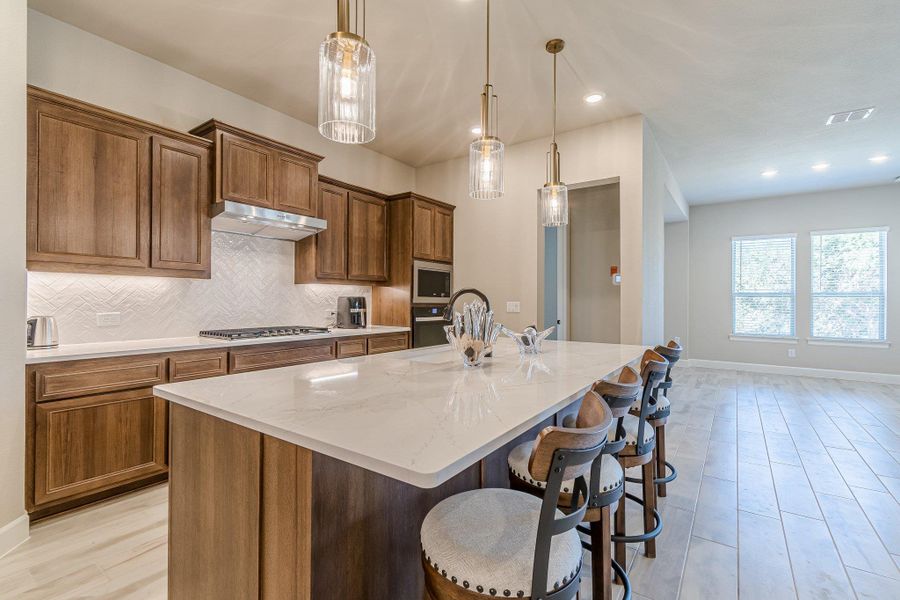 Kitchen featuring under cabinet range hood, stainless steel appliances, a breakfast bar, decorative backsplash, and a center island with sink