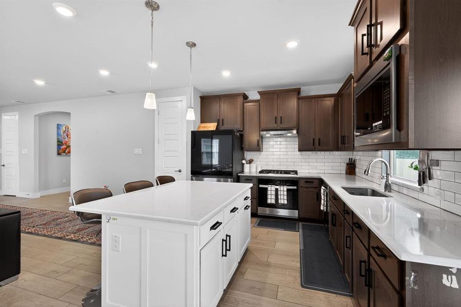 The kitchen features a white island with a countertop, dark wood cabinetry, stainless steel appliances, and a white subway tile backsplash