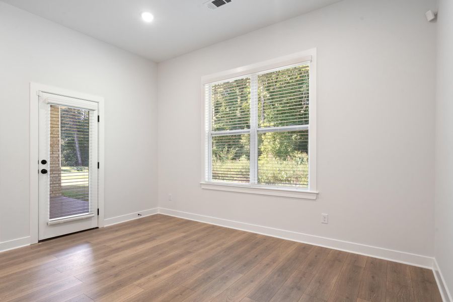 Wood-finish flooring, white painted walls, recessed ceiling light, transom window above a glass-paneled door, and a multi-pane window with white blinds