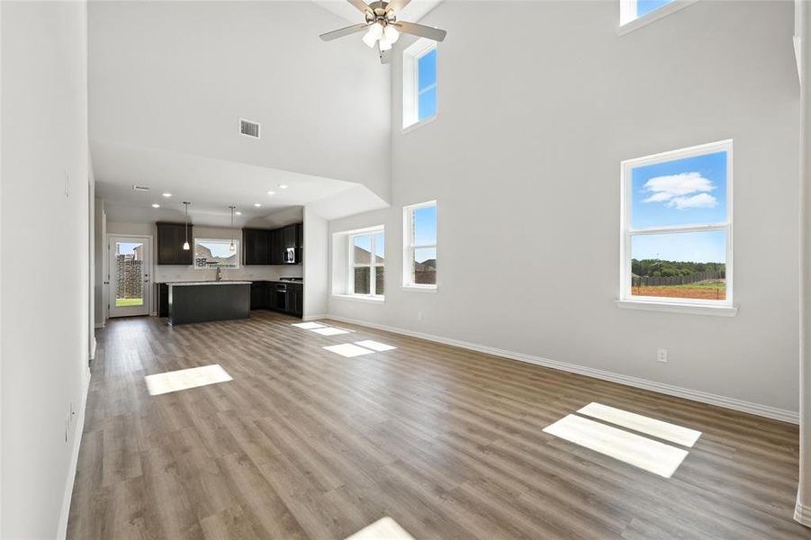 Unfurnished living room with a towering ceiling, wood finished floors, and a ceiling fan Unfurnished living room with a towering ceiling, wood finished floors, and a ceiling fan